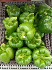 Green bell peppers in a wicker basket on a market stall.
