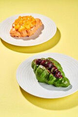 Two croissants, one with mango and the other with pistachio and cherries, are served on white plates against a yellow background.