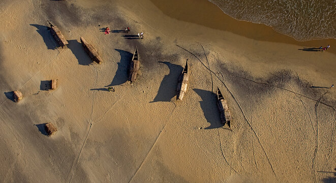 Kovalam, India - 15 February 2007: Aerial view of fishing boats resting on the sandy shore, their dark forms casting long shadows against the golden sand near the gentle ocean waves.