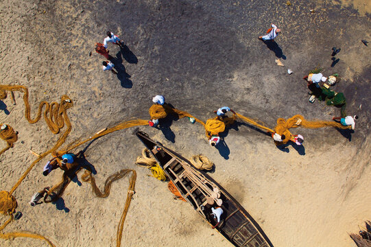 Kovalam, India - 15 February 2007: Aerial view of fishermen hauling nets from the sandy shore near Kovalam, their vibrant clothes a stark contrast to the earthy tones.