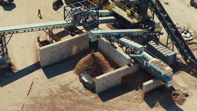 Aerial drone view of dirt sortiment falling at an outdoor construction waste sorting facility on a sunny day with dust
