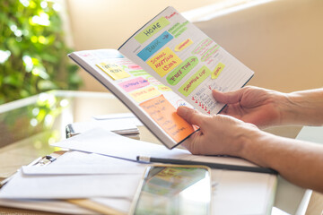 Woman managing her weekly schedule using colorful sticky notes and handwriting in her agenda, highlighting her organizational skills and busy life filled with various appointments and tasks