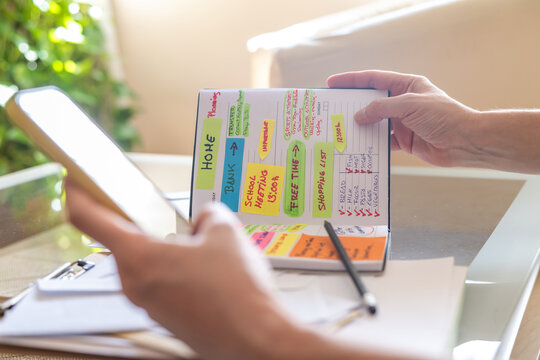 Woman managing her daily schedule using colorful sticky notes on a notebook, consulting her digital tablet for appointments and errands, demonstrating effective organization and time management