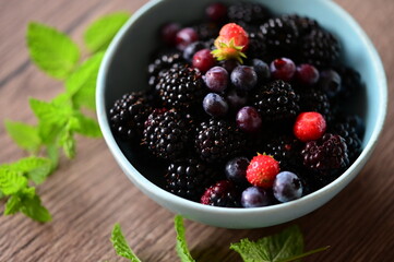Close-up macro view of a bowl with fresh seasonal fruits — blackberries, blueberries, and mint. A vibrant and healthy mix of summer berries, perfect for fresh eating, healthy lifestyle, and food photo