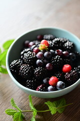 Close-up macro view of a bowl with fresh seasonal fruits — blackberries, blueberries, and mint. A vibrant and healthy mix of summer berries, perfect for fresh eating, healthy lifestyle, and food photo