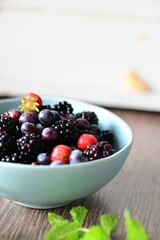 Blue bowl filled with fresh summer fruits, including ripe blueberries and blackberries, set against a clean white background.