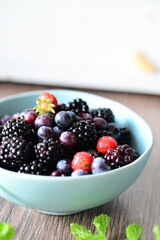 Blue bowl filled with fresh summer fruits, including ripe blueberries and blackberries, set against a clean white background.