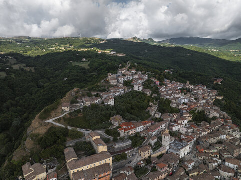 Aerial view of ancient rooftops cascading down the hillside amidst verdant forests under a cloudy sky, Morcone, Benevento, Campania, Italy.
