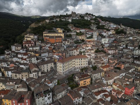 Aerial view of terracotta rooftops cascading down the hillside toward the winding streets and historic buildings under a cloudy sky, Morcone, Benevento, Campania, Italy.