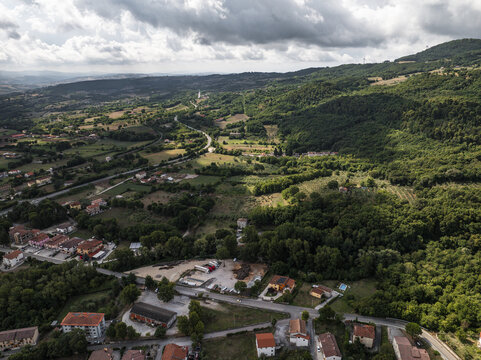 Aerial view of a village nestled amidst rolling hills and verdant forests, with the sky a dramatic canvas of light and shadow, Morcone, Benevento, Campania, Italy.
