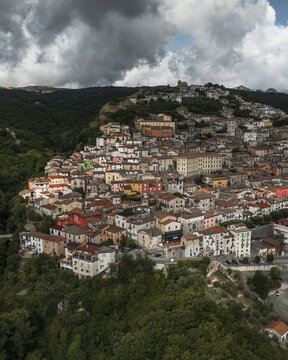 Aerial view of the ancient town cascading down a hillside under a dramatic sky, blending terracotta rooftops with lush greenery, Morcone, Benevento, Campania, Italy.