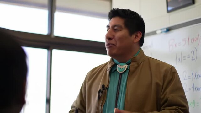 smiling indigenous male teacher in classroom in front of whiteboard speaking. man teaching children. native american heritage day, education. back to school