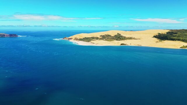 Aerial view of the rugged Omapere coastline, where the deep blue ocean meets the sandy beach and lush greenery, Omapere, Northland Region, New Zealand.