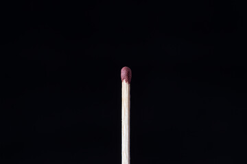 A single matchstick standing upright against a solid black background.