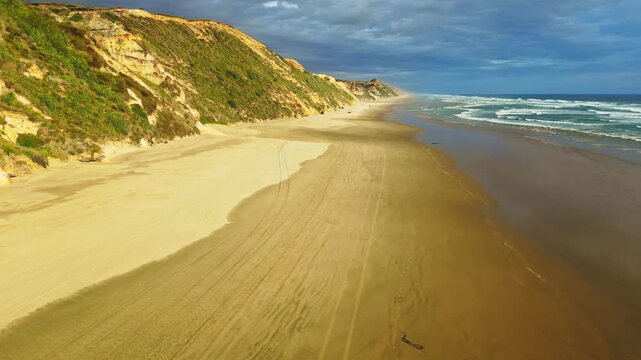 Aerial view of sandy beach meeting the ocean, alongside vegetated dunes under a cloudy sky, creating a serene coastal scene, Dargaville, Northland Region, New Zealand.