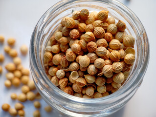 dried coriander seeds spill from a glass jar onto a white surface, creating a beautiful pattern with warm, earthy tones.