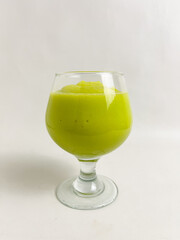 Green-colored avocado smoothie in a wine glass on a white table