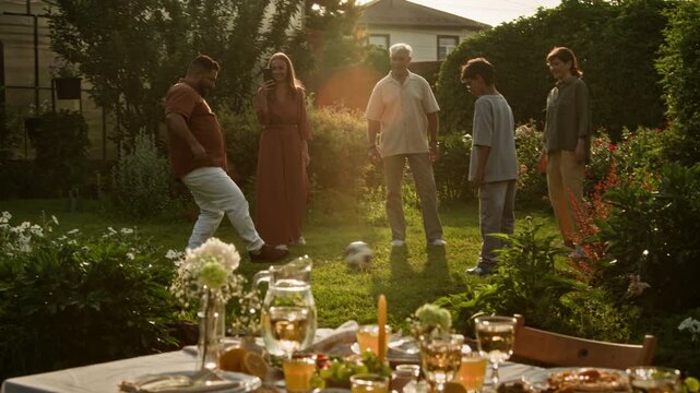 Idyllic wide angle shot of big multigenerational family playing with ball together outdoors in picturesque garden lit by sunlight, lens flare effect