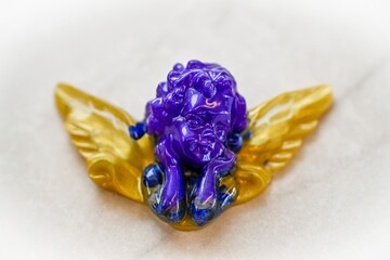 High resolution color image of a beautiful and colorful angel mage of epoxy resin in purple and golden colors with a white marble background- Israel