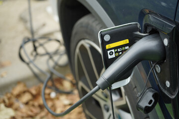 Detalle de coche el&eacute;ctrico aparcado en la calle con el puerto de carga abierto y un enchufe y cable para cargar la bater&iacute;a