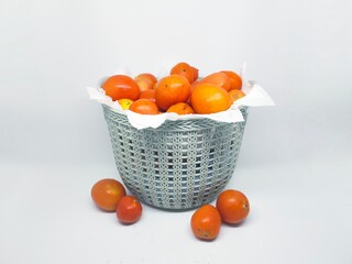 A basket filled with ripe, orange tomatoes, with some scattered around. Set against a clean white backdrop, perfect for food-related projects.