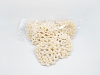 Close-up shot of a pile of kerupuk crackers in a transparent plastic bag, isolated on a white background. These delicious snacks are ready to be enjoyed.