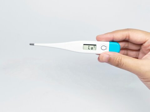 A hand holds a digital thermometer indicating a low temperature reading. This image represents health, medical care, and temperature measurement.