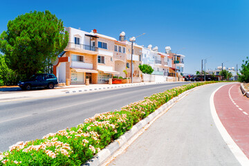 Fototapeta premium Colorful houses in the Mediterranean resort of Polis in Cyprus. Landscape of the island town with an empty road and bike path.