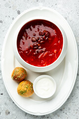 Red bean soup with vegetables served in a bowl, accompanied by garlic bread rolls and sour cream on a white plate over a speckled gray surface