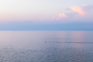 calm sea under sunset sky in soft pastel colors with lonely boat. sea waterline with clean horizon. sea water surface