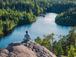 A man sits on a rock and contemplates a forest lake