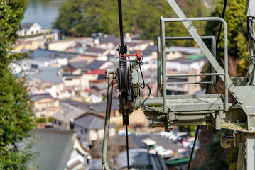 Close-up view of a cable car pulley system with a backdrop of a town and greenery