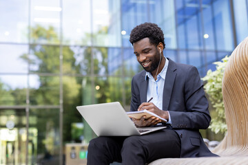 Business professional sitting outdoors, using a laptop and notebook, enjoying productive work connections.