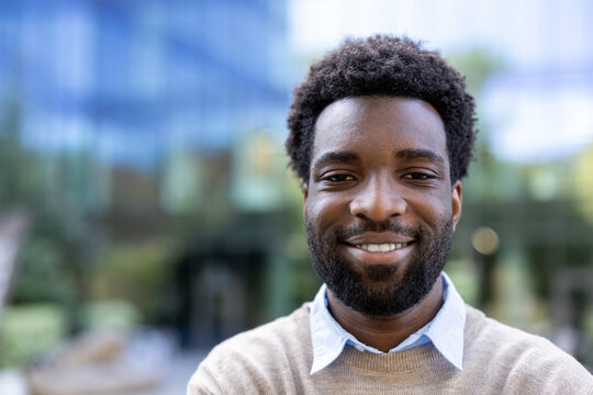 A portrait of an individual outdoors, exuding confidence and warmth with a cheerful demeanor. This image highlights personal charm and positivity against a vibrant urban background.