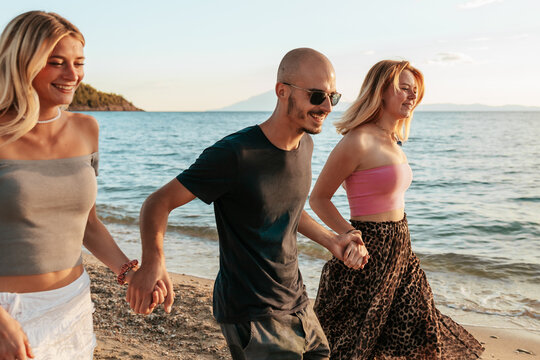 Friends holding hands walking on the beach at sunset in Potos, Thassos