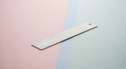 A blank silver metal bookmark with decorative etched floral pattern rests diagonally on a pastel background