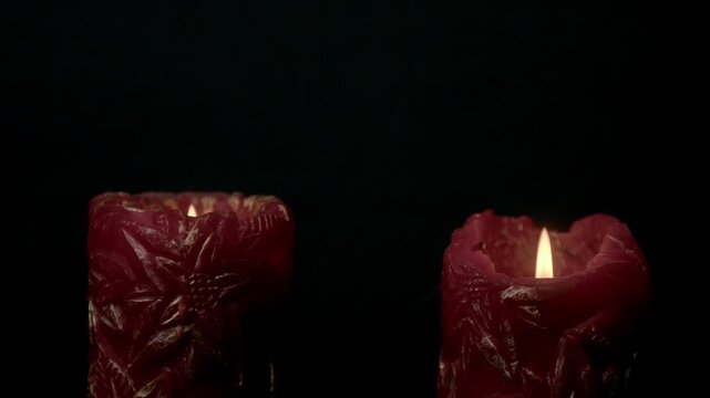 Close-up shot of two red candles with intricate designs and rising smoke against a black backdrop, symbolizing the concept of death or endings. Dramatic, moody lighting sets a somber tone.