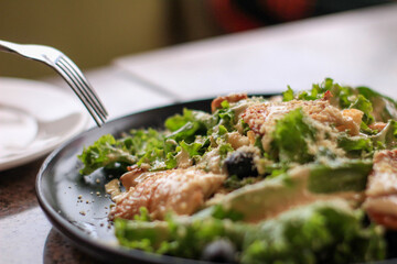 A close-up view of a garden salad featuring crisp green lettuce, scattered black olives, and a generous sprinkle of grated cheese on top, served on a dark plate.