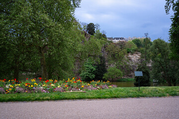 Scenic view of Parc des Buttes-Chaumont in Paris, France, with colorful flower beds, lush green trees, rocky cliffs, and serene lake on a spring day