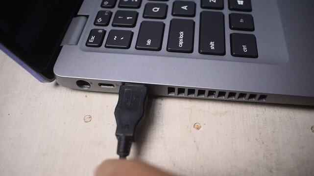 Close up of a woman's hand plugging a USB cable into a port on a laptop with focus
