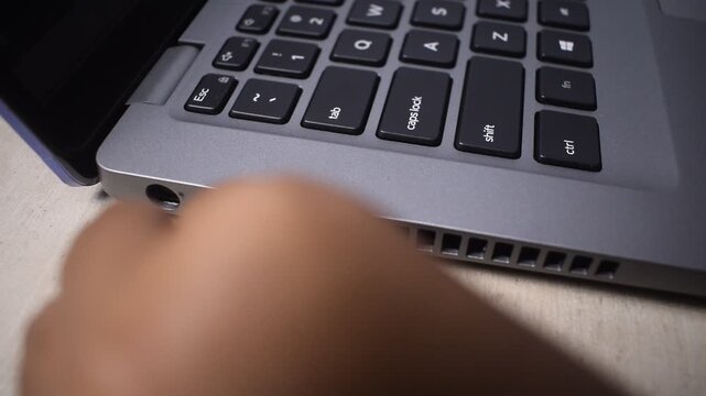 Woman's hand plugging a USB cable into a port on a laptop with focus