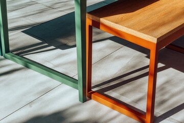 Outdoor furniture detail, wooden tabletop,  green and orange metal legs,  sunlight shadows on light gray tile