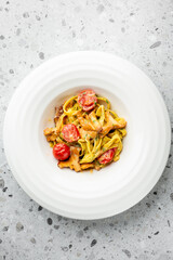 Creamy pasta with chanterelle mushrooms and cherry tomatoes, garnished with herbs, served on a white plate over a gray speckled background.