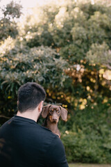Man with black hair and wearing black holding and cuddling a brown dachshund. Love your pet, dog, companion
