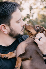 Man with black hair and wearing black holding and cuddling a brown dachshund. Love your pet, dog, companion