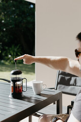 Man pouring filter coffee from a french press into a white cup at an outdoor table