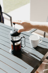 Man pouring filter coffee from a french press into a white cup at an outdoor table