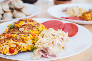 A plate filled with a colorful vegetable omelet, creamy spaghetti carbonara, and round slices of salami on a wooden table, Delicious Home Meal.