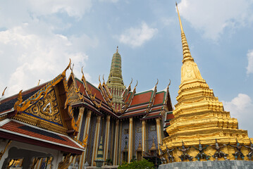 Fototapeta premium Ornate golden chedi and intricate temple architecture of the Grand Palace in Bangkok, Thailand under a partly cloudy sky, showcasing rich cultural heritage. Sacred landmark.