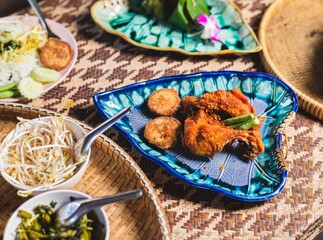 Traditional Asian fried chicken meal with crispy patties, fresh bean sprouts, and vegetables served on a woven mat and vibrant leaf-shaped plates, authentic dining.